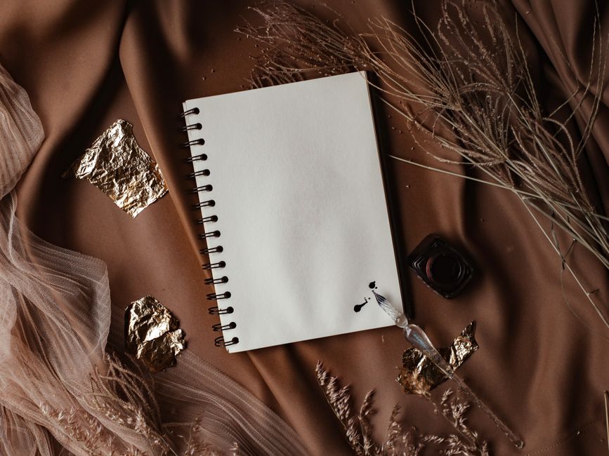 Top view of a blank notebook with ink bottle, surrounded by natural elements on brown fabric.