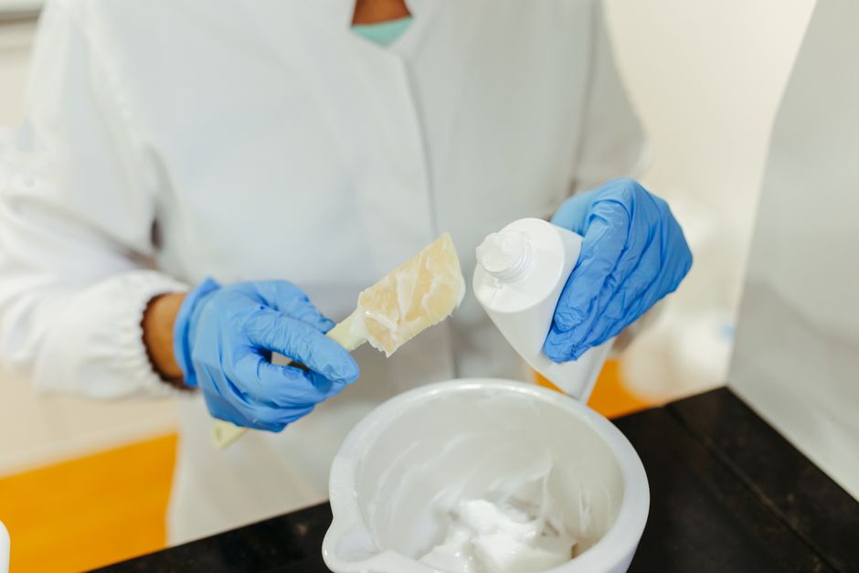A lab technician wearing gloves mixes skincare cream with precision for research purposes.