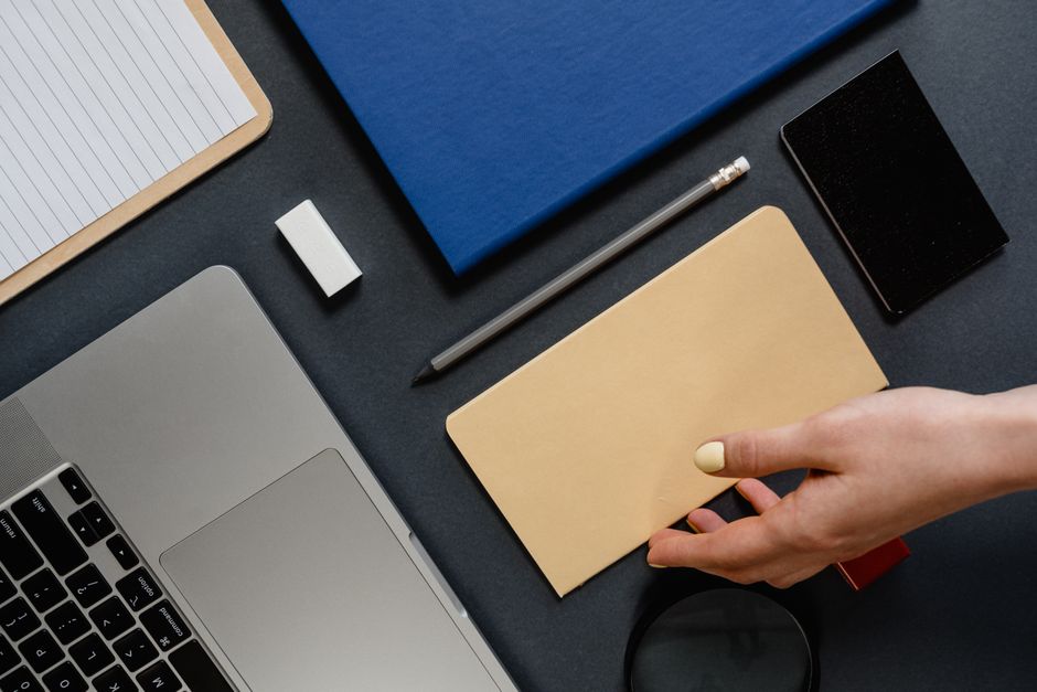 A clean and tidy office desk setup with a laptop, stationery, and a hand picking up an envelope.